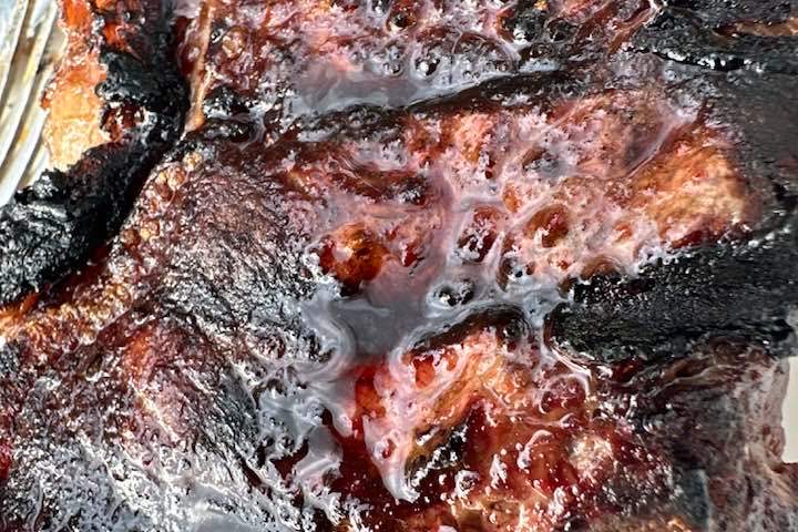 Close-up of a charred grilled meat with a glossy texture and grill marks.