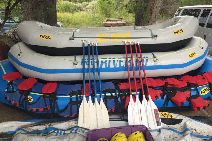 Stacked inflatable rafts with paddles and life jackets in an outdoor setting.