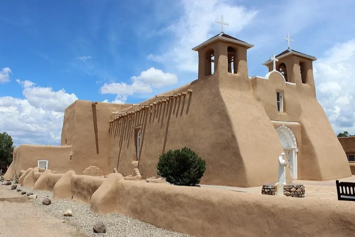 Adobe church with twin bell towers against a blue sky with clouds.